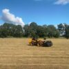 JM Agri Design TR-8 Bale Handler lifting bales in a field using a loader on a sunny day.